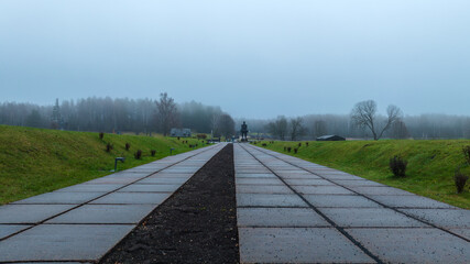 Foggy memorial walkway leading to a dark statue in Belarus