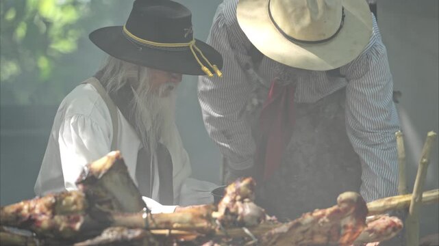 Group of cowboys preparing food at a campfire, roasting meat together in a warm and rustic outdoor setting