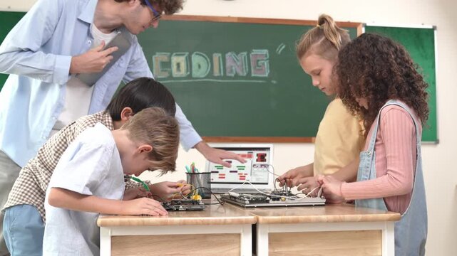 Group of diverse student working together on main board with laptop screen display engineering prompt written while teacher hold tablet and explain online software at STEM technology class. Pedagogy.