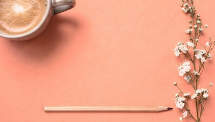 Minimalist flat lay with a cup of coffee, pencil, and white flowers on a soft peach background.