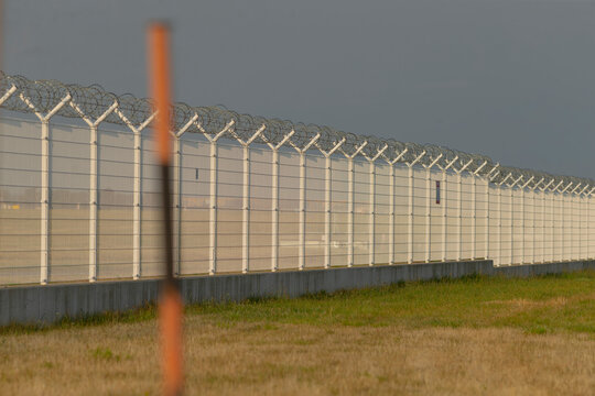wide perimeter fence with razor coils conveying deterrence and exclusion, foreground marker posts adding depth, atmosphere