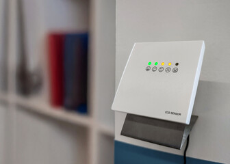 CO2 sensor with color coded indicator lights, visual warning system for monitoring air quality and ventilation needs. Carbon dioxide sensor with yellow warning lights in office, ventilate workspace.