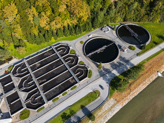 Aerial view of a wastewater treatment facility with circular tanks and green forest areas highlighting innovative technology for urban water management.
