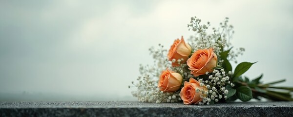 Bouquet of orange roses with baby breath flowers rests on granite surface. Overcast sky creates somber mood, peaceful remembrance setting. Floral tribute signifies love loss.