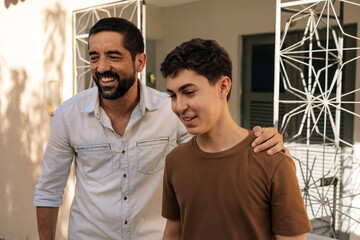 Father places his hand on his teenage son’s shoulder while talking outdoors, expressing emotional support, trust, empathy, and a strong parent-child bond focused on wellbeing and mental health