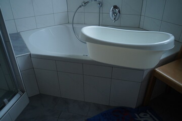 White bathtub with wall-mounted oval sink and shower hose in a tiled bathroom. Clean minimalist interior.