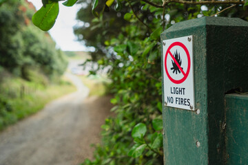 Small Light No Fires warning sign on gatepost in front of unpaved road leading to a beach and sea. ...