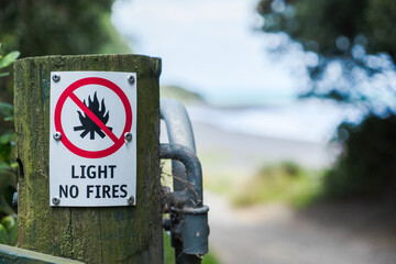 Small Light No Fires warning sign on gatepost in front of unpaved road leading to a beach and sea. ...