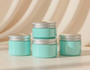 Four stacked mint green cosmetic jars with silver lids on a light background. The jars are empty and designed for skincare products.