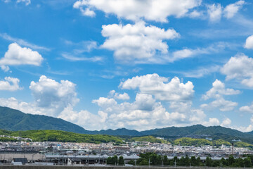 夏の青空と白い雲、山の緑と街並みのパノラマ