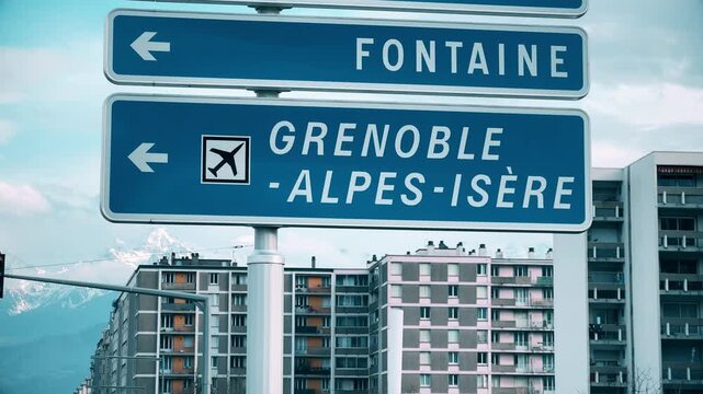 Road signs pointing to Grenoble Alpes Isere airport with alpine mountains and urban buildings