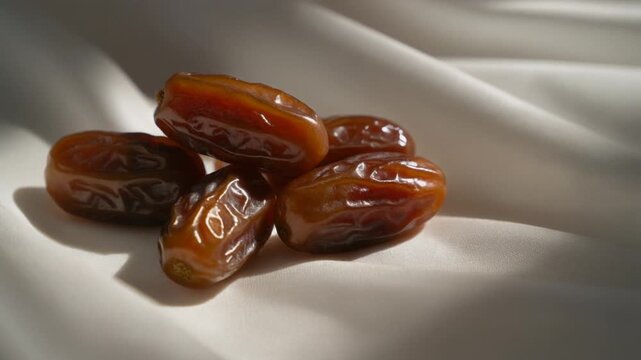 Cinematic close-up of glossy dates on white matte fabric with soft directional lighting. Healthy organic snack.