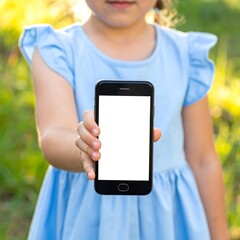 A little girl in blue holds a phone with a white screen, focused in on the screen against a blurred outdoor backdrop