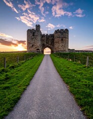 A long pathway leads to an old stone castle under a colorful sunset sky