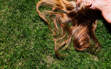 Relaxation: Young Woman Enjoying Daybreak with Long Hair Spread on Fresh Green Grass Outside copy-space