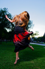 Joyful Movement: Young Woman Dancing with Long Hair Flowing Outside in Vibrant Dress Captured in Park Setting at Twilight