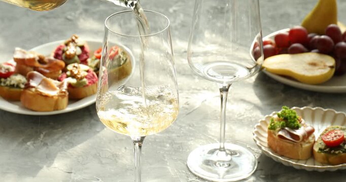 Pouring wine into glasses on table with bruschette, grapes and pears