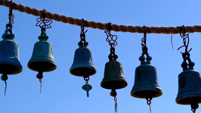 Several bronze bells hang suspended from a thick rope against a clear blue sky