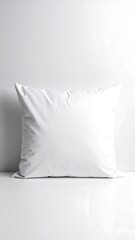 A plain white pillow is resting against a white wall on a glossy white surface, lit evenly