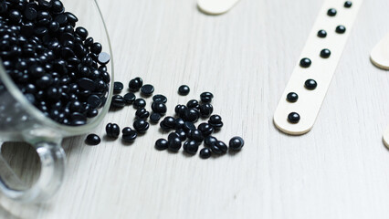 Black hard wax beans scattering across wooden surface, wooden applicators nearby, preparing for professional hair removal and skin smoothing treatment