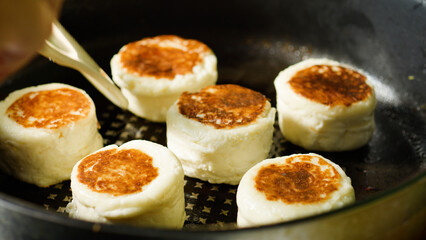 Golden brown syrniki sizzling in skillet, chef turning crispy cottage cheese pancake with metal tongs, browning surface glistening