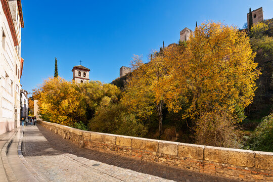 The Alhambra rises above the historic Carrera del Darro street along the Darro River in the old town of Granada, Spain at Autumn with the Iglesia de San Pedro y San Pablo church behind.