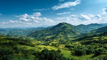 Fototapeta premium Vast green mountain range under a bright blue sky with white scattered clouds