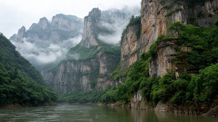 Majestic steep rocky cliffs covered in lush green vegetation rise above a calm river under a misty sky