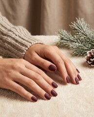 Close-up of elegant hands with matte dark red manicure on a cozy winter background
