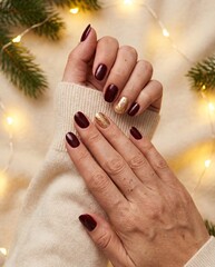 Cozy festive winter manicure on hands with elegant nails, surrounded by lights and pine