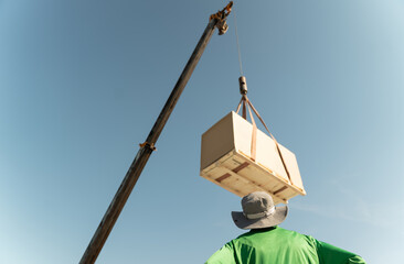Crane lifts large box at construction site under clear blue sky with worker observing the process