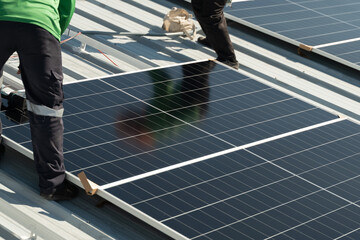 Workers install solar panels on a metal roof during daylight hours in a clear sky, focusing on the clean energy project with multiple panels