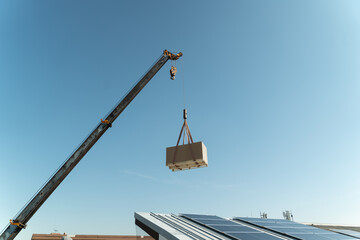 Construction crew lifts large container with crane at building site under blue sky during daylight hours