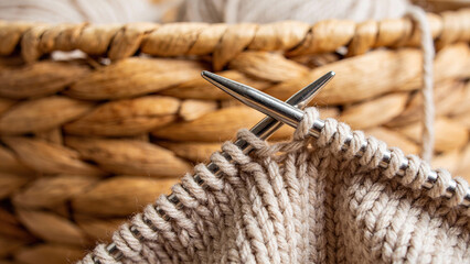 Knitting needles working on beige yarn in a woven basket  