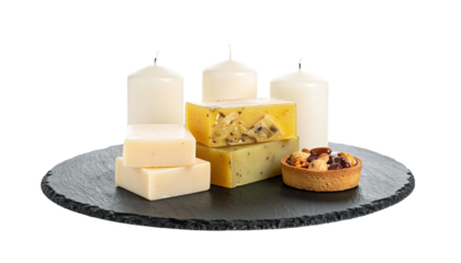 Arrangement of candles, soaps, and a tart on a dark slate surface