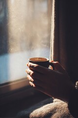 Hands holding steaming hot beverage indoors