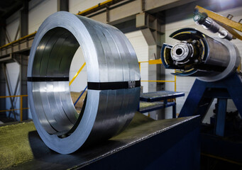 Metal coil placed on machinery for processing in an industrial facility.  The equipment is used for shaping and cutting metal materials. The setting is a large, industrial space.