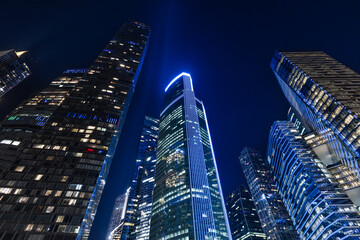 City skyline at night with tall buildings and glowing lights in a modern urban setting. Skyscrapers stand tall at night, illuminated by bright lights. The scene showcases atmosphere of the city.