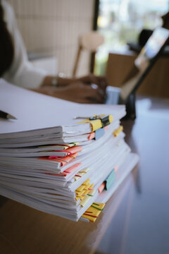 Close-up of a businesswoman&rsquo;s hands reviewing a large stack of organized documents with paper clips at an office desk, representing heavy workload, administration, and paperwork management.