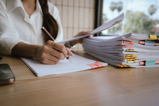 A businesswoman holding a smartphone and a thick stack of documents at an office desk, symbolizing multitasking, heavy workload, administration, and modern business management.