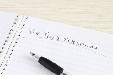 Close up shot of handwriting "New Year's Resolutions" on new notebook with black pen on white wooden table.