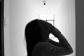 A lonely young woman sits on the floor in a narrow hallway, clutching her head in despair, expressing sadness, stress, and emotional conflict in the quiet, simple interior of the building. The image i