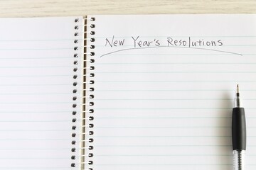 Close up shot of handwriting "New Year's Resolutions" on new notebook with black pen on white wooden table.