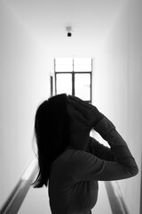 A lonely young woman sits on the floor in a narrow hallway, clutching her head in despair, expressing sadness, stress, and emotional conflict in the quiet, simple interior of the building. The image i