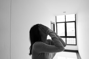 A lonely young woman sits on the floor in a narrow hallway, clutching her head in despair, expressing sadness, stress, and emotional conflict in the quiet, simple interior of the building. The image i