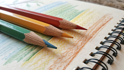 Three colored pencils lying on a spiral sketchbook with swatches of color drawn on the page