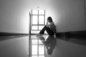 A lonely young woman sits on the floor in a narrow hallway, clutching her head in despair, expressing sadness, stress, and emotional conflict in the quiet, simple interior of the building. The image i