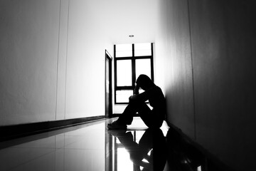 A lonely young woman sits on the floor in a narrow hallway, clutching her head in despair, expressing sadness, stress, and emotional conflict in the quiet, simple interior of the building. The image i