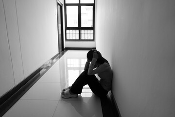 A lonely young woman sits on the floor in a narrow hallway, clutching her head in despair, expressing sadness, stress, and emotional conflict in the quiet, simple interior of the building. The image i