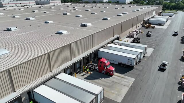 Large industrial building logistics center with trucks at loading docks aerial view